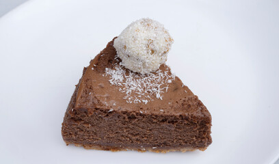 Sweet dessert. Closeup view of a slice of chocolate cheesecake with a coconut truffle, in a white plate.	
