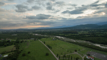 Idyllic rural landscape. Aerial view of the pirvate community residences, green field and river flowing across the hills and forest under a magical sunset sky. 