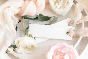 Cards near light pink fabric and cream flowers on plate close up, copy space, wedding mockup