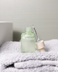 Obraz na płótnie Canvas Opened cosmetic bottle with green serum on folded bath towel against basin close up
