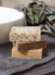 Handmade beige soap bars on dark grey towels, near plant and basin in bathroom, mockup