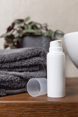 White blank pump cream bottle near grey towels, plant and basin on wood in bathroom, mockup
