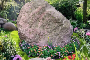 Beautiful garden, a huge stone stands on the grass, the stone surface is smooth and clean, at the bottom of the stone grows a circle of flowers and plants, the sun shines brightly, quiet and beautiful