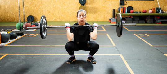 A woman in her 40s and 50s is working out inside a gym.The middle-aged woman does a squat with a...