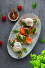 Toast bruschetta with grilled asparagus, poached egg, strawberry and fresh cream cheese. Sourdough bread with vegetables and egg. Food photography. Healthy breakfast, brunch. Summer food