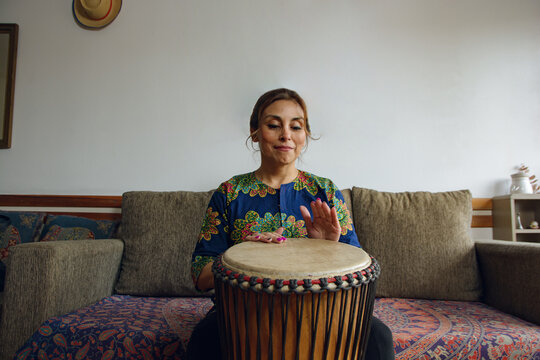 wide angle front view of a Woman sits at home playing a Djembe drum