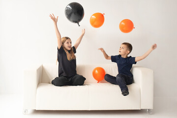 a boy and a girl in a large bright room play with black and yellow balloons in the colors of Halloween. White background