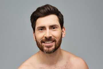 A bearded man stands shirtless, showcasing his facial hair with confidence.