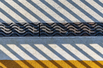 Late afternoon image of an ornamental metal trench drain in concrete with shadow pattern from an adjacent ornamental fence.