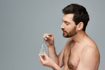 A shirtless man holds a bottle of serum.