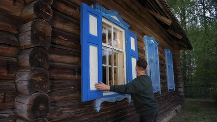 a man opens the shutters on a window in an old wooden house.  - Powered by Adobe