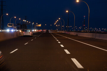 Nighttime highway scene - vehicles in motion - illuminated streetlights - dark blue sky backdrop....