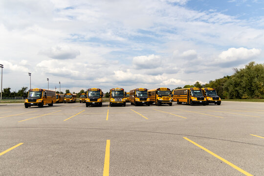 Yellow school buses lined up in an empty parking lot - under a partly cloudy sky. Taken in Toronto, Canada.