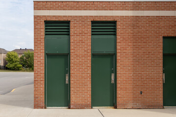 Three green doors - set in red brick wall adjacent to empty parking lot - distant houses and trees...