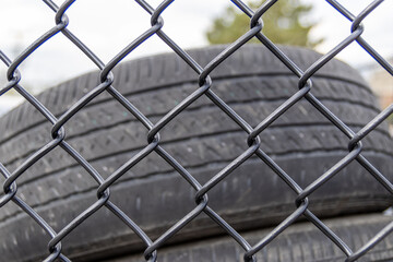 Fototapeta premium Stacked used tires - behind chain-link fence - under cloudy sky. Taken in Toronto, Canada.