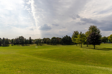 Vast green grassy field - partly cloudy sky - scattered trees - soft shadows - white goal post and...