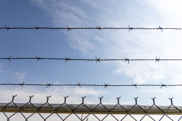 Barbed wire fence - clear sky backdrop - security boundary - restricted area - minimal cloud cover. Taken in Toronto, Canada.
