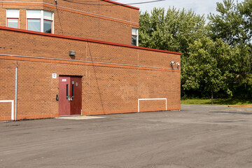 Brick building with red door - empty parking lot - green trees background. Taken in Toronto, Canada.