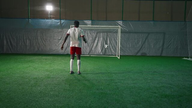 Black soccer player exercising penalty in training hall, scoring goal, back view