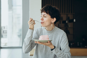 Woman closed her eyes with pleasure, enjoying a piece of cake in a modern cafe.