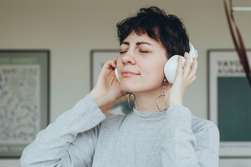A woman wears white headphones and listens to music with her eyes closed.