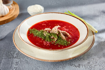 Classic beetroot borscht with beef and a dollop of sour cream, presented in a speckled bowl on a grey textured backdrop