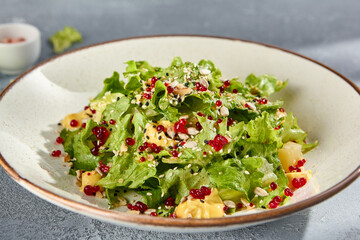 Green salad with pineapple chunks and pomegranate seeds, fresh and colorful in a speckled bowl