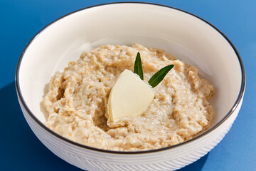 Creamy Oatmeal with Butter in White Bowl on a Blue Background - Nutrition and Breakfast