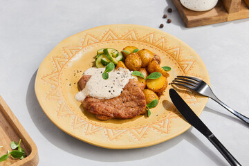 Delicious Pork Chop with Potato Wedges and Creamy Sauce on Artisanal Plate