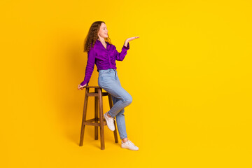 Full body photo of pretty young girl sit chair hold look empty space wear trendy violet outfit isolated on yellow color background - Powered by Adobe
