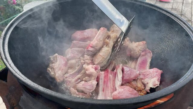 Fried meat in a wok on fire is stirred with a spatula, close-up. Mouth-watering chunks of pink beef or pork fried in oil vat on fire, the concept of fatty food