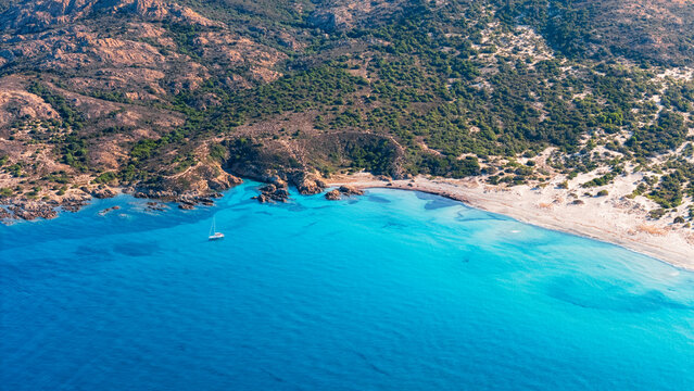Aerial drone view of sailing ship in front of Plage de l'Ostriconi, Mediterranean beach during summer, island of Corsica, France.