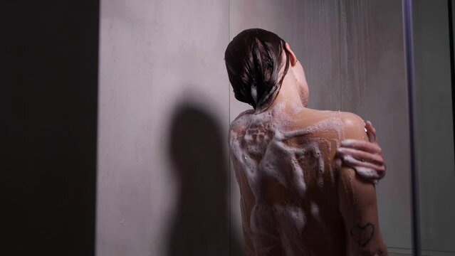 Woman with foam on her skin taking shower in bathroom, back view