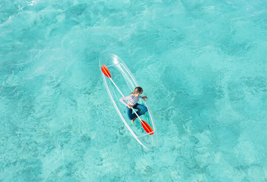 Aerial view of turquoise waters with woman paddling on a glassboat, Thoddoo, Maldives.