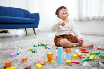 child girl feeling happy and playing with colorful toy blocks on the carpet floor