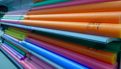 Brightly colored pool noodles neatly stacked on display shelves in a store