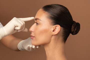 Cosmetology, plastic surgery and beauty concept. Surgeon hands touching woman nose, consulting...
