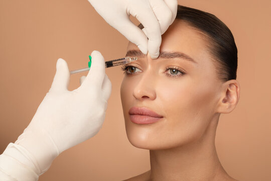 Beautician making hyaluronic acid injection for glabella facial rejuvenation procedure, young European woman getting cosmetic injection between eyebrows