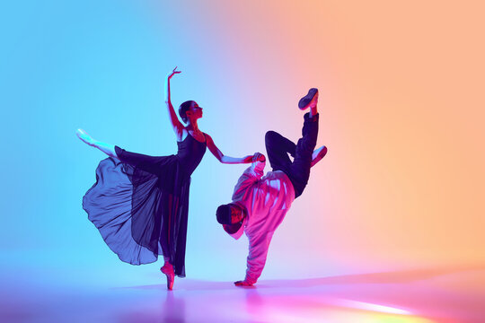 Ballet and street dance mix. Beautiful young girl in black dress, ballerina dancing with young man, hip hop performer on gradient background in neon. Concept of classical and modern dance, performance