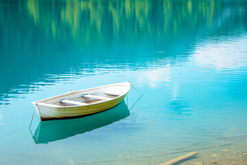 Obraz premium Small white rowboat anchored in clear blue water, surrounded by lush green foliage.