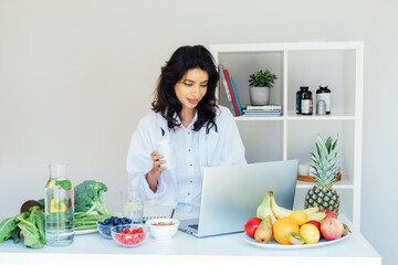 Positive Indian female nutritionist having online consultation with client at office desk with...