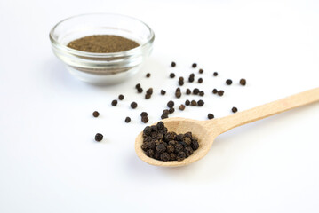 Ground pepper and peppercorns in a wooden spoon close-up on white.