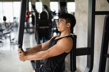 A determined man in a black tank top uses a chest press machine in a modern gym. His focus and...