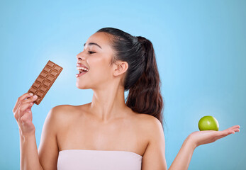 Girl, chocolate and apple in studio for eating or unhealthy choice on cheat day for sweet snack or...