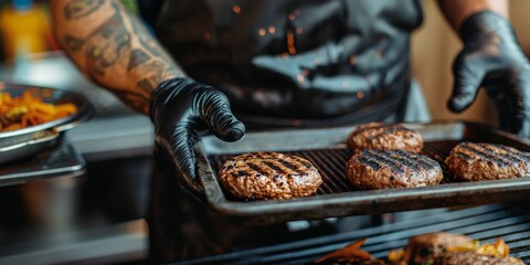 Close up male chef in an black apron holding a tray of grilled burger patties. Barbecue grill party or catering kitchen.