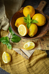 Fresh yellow lemons in a glass and wooden plate with fresh green  leaves of mint