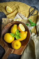 Fresh yellow lemons in a glass and wooden plate with fresh green leaves of mint