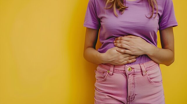 Close up of a woman with stomach pain holding her belly isolated on a yellow background, a female feeling hangover or stomach burning