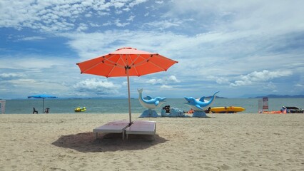 Beautiful tropical scenery, two sun beds and orange umbrella. White sand, blue sky clouds at Mui Nai beach, Ha Tien, Vietnam in summer.