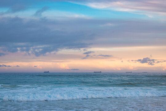 Cargo ships lined up at sea en route to Newcastle Harbour under a vibrant sunset sky